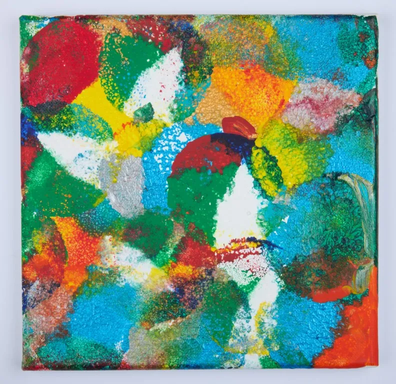 A small, square abstract painting with a highly textured surface. The painting is a patchwork of colors, including vibrant red, blue, green, yellow, and orange, with some white and metallic silver. The colors are applied in large, overlapping circular and splotchy shapes. The texture suggests a stippling technique, with many small, raised dots of paint.
