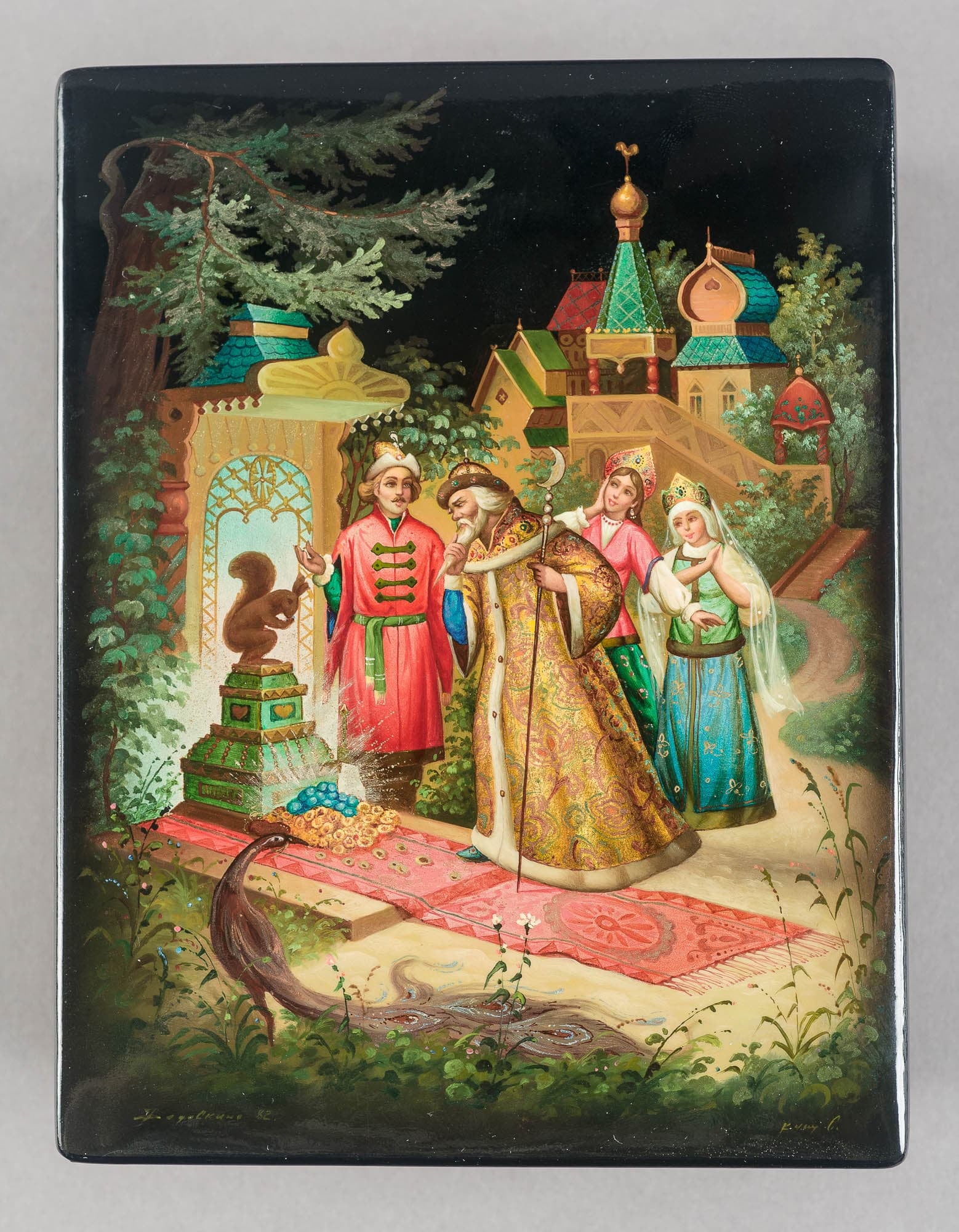 A lacquered box featuring a detailed painting of a scene with people in traditional attire, surrounded by ornate buildings and lush greenery. The intricate details and vibrant colors bring the scene to life.