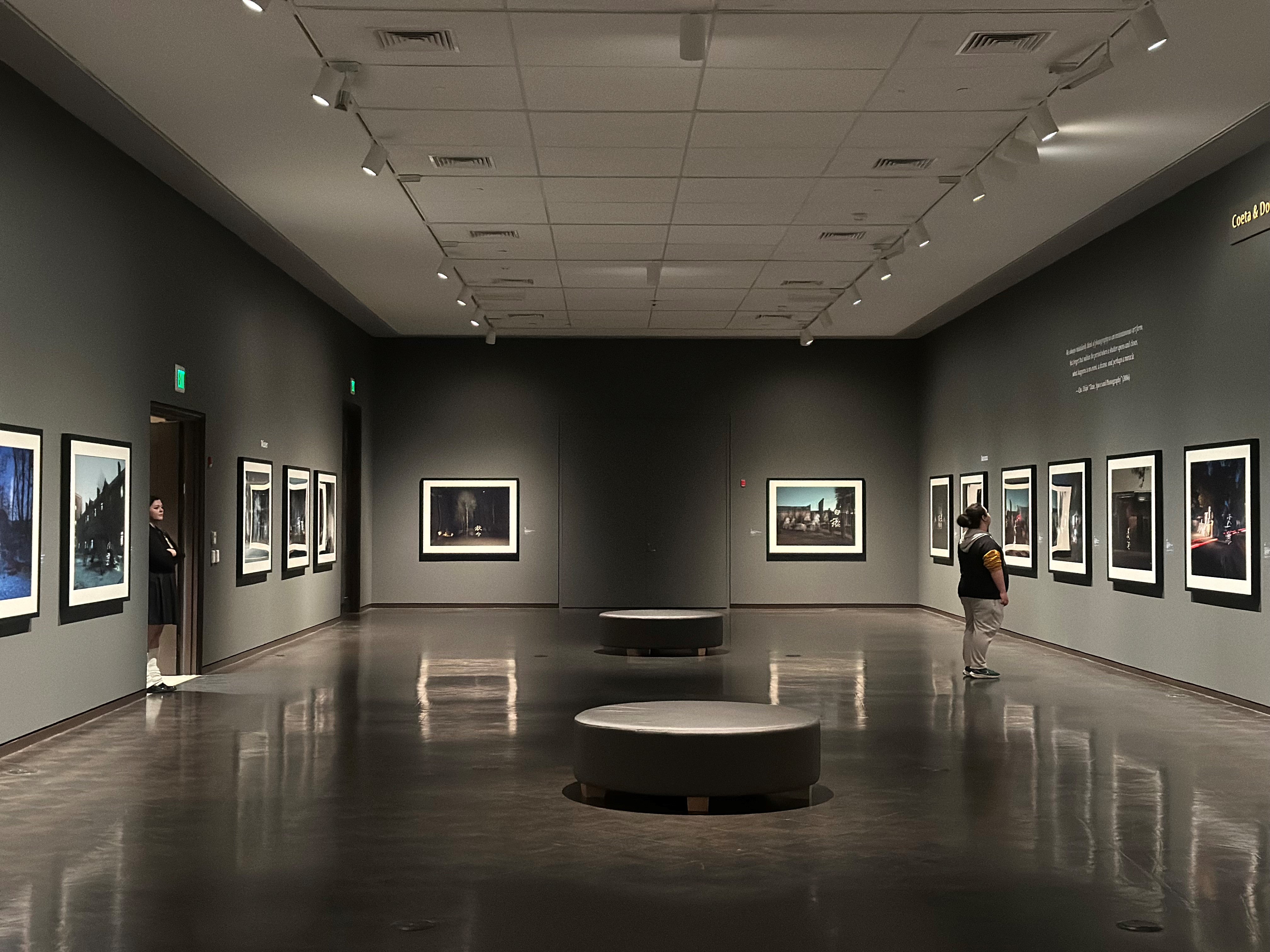 Large photographs hang on dark gray walls in the Barker Gallery of the JSMA.