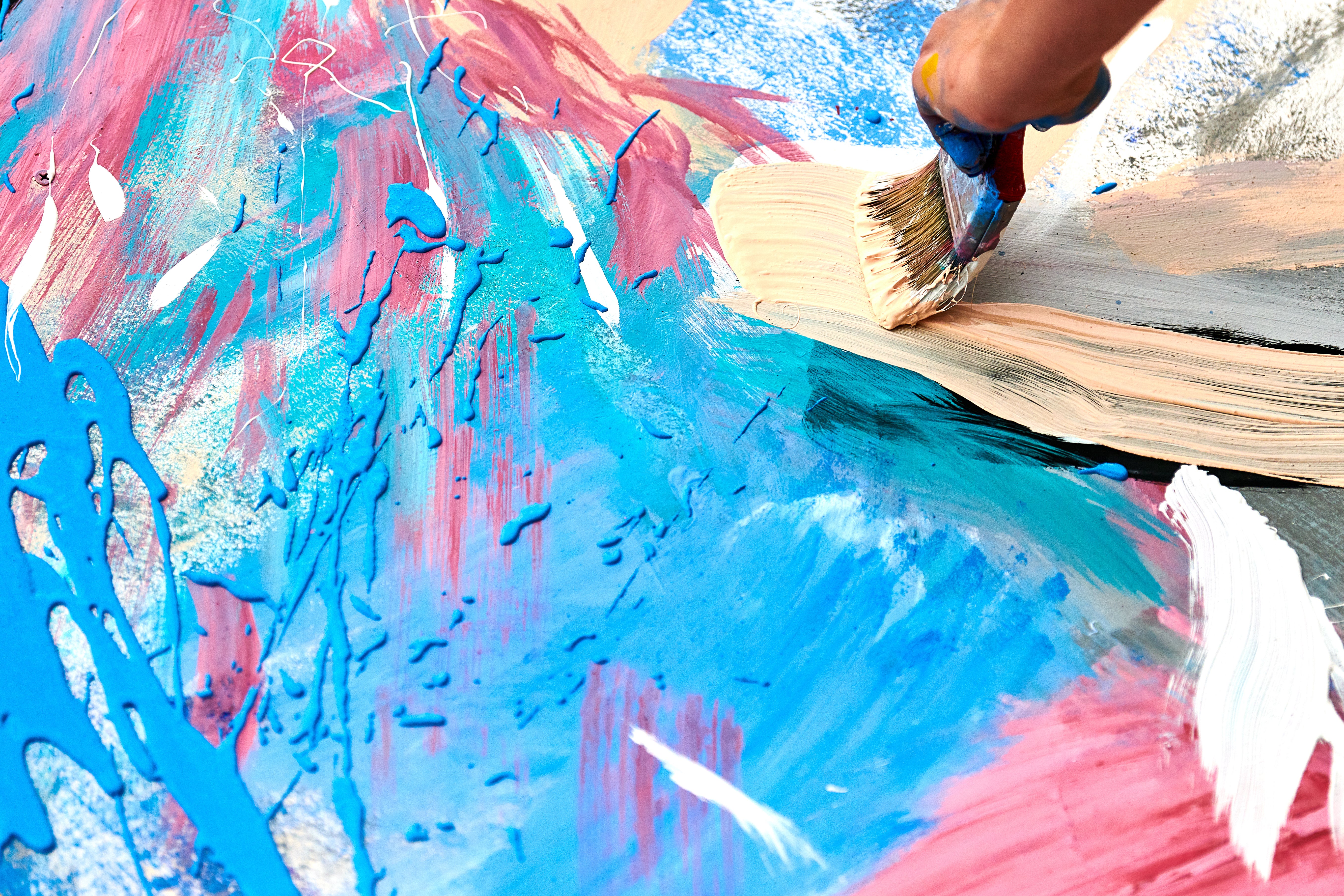 A hand uses a paint brush to create a blue and pink canvas