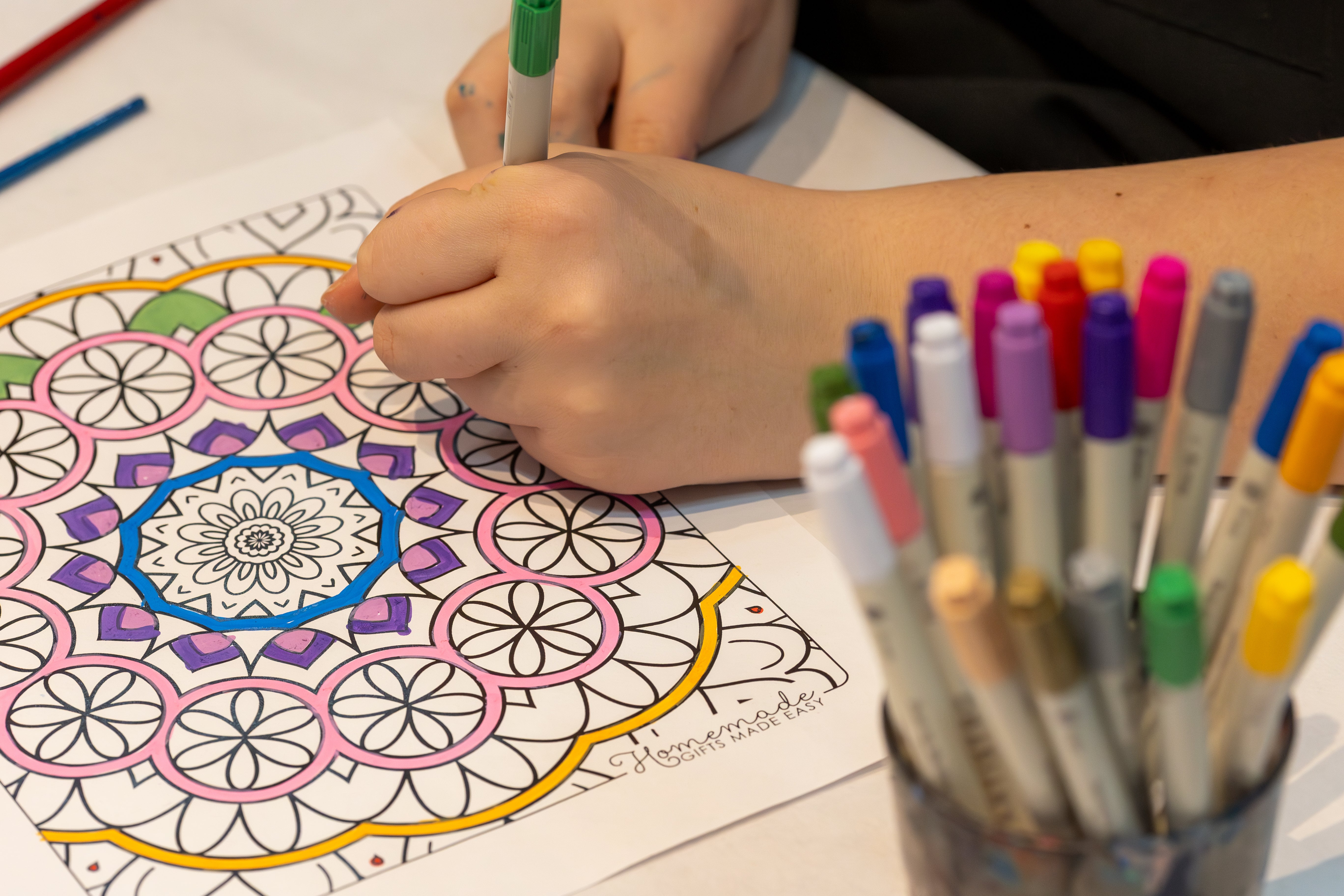 Hands use a blue color marker to color a pattern.