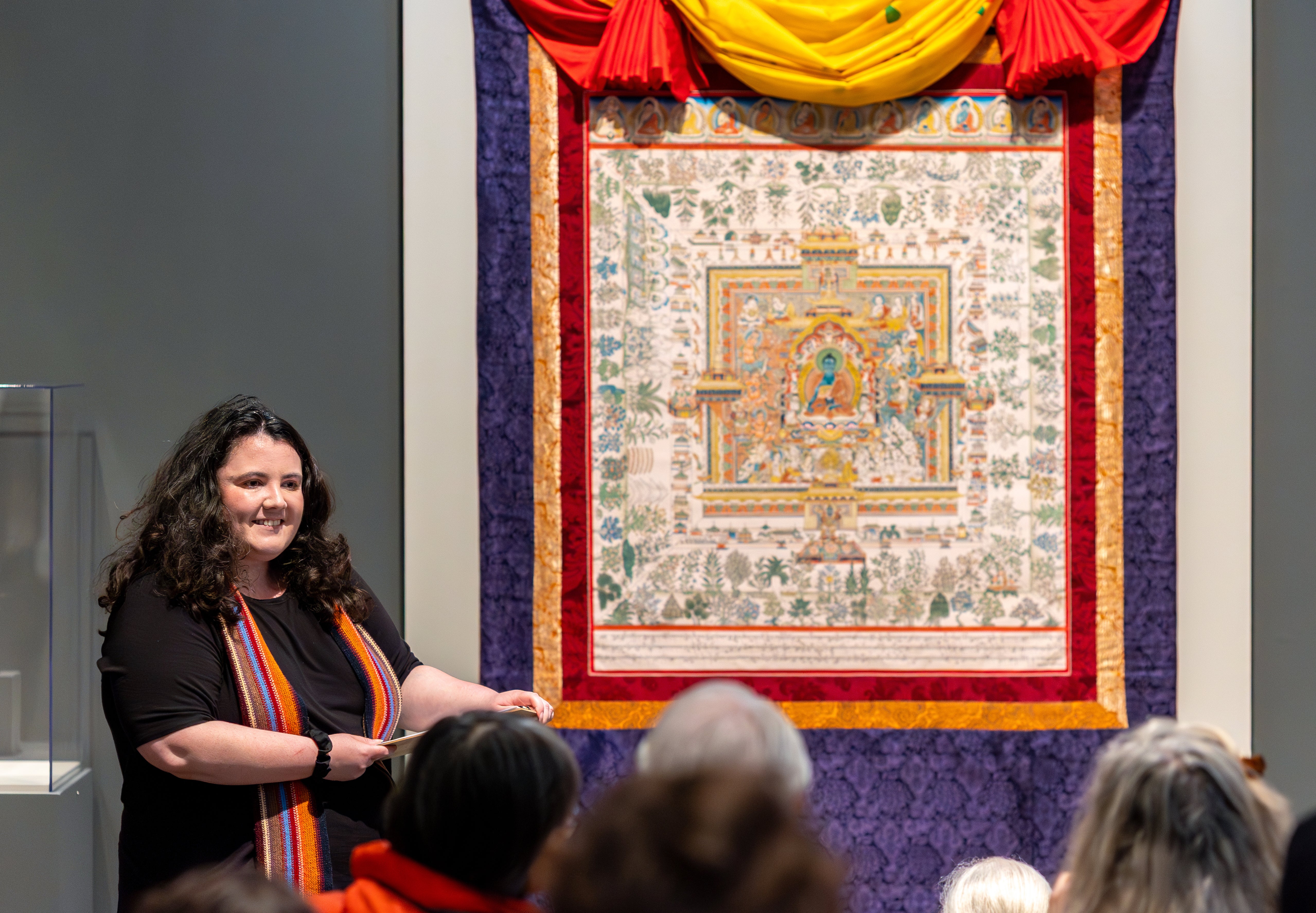 A woman standing next to a work of art is talking to a group of people. 