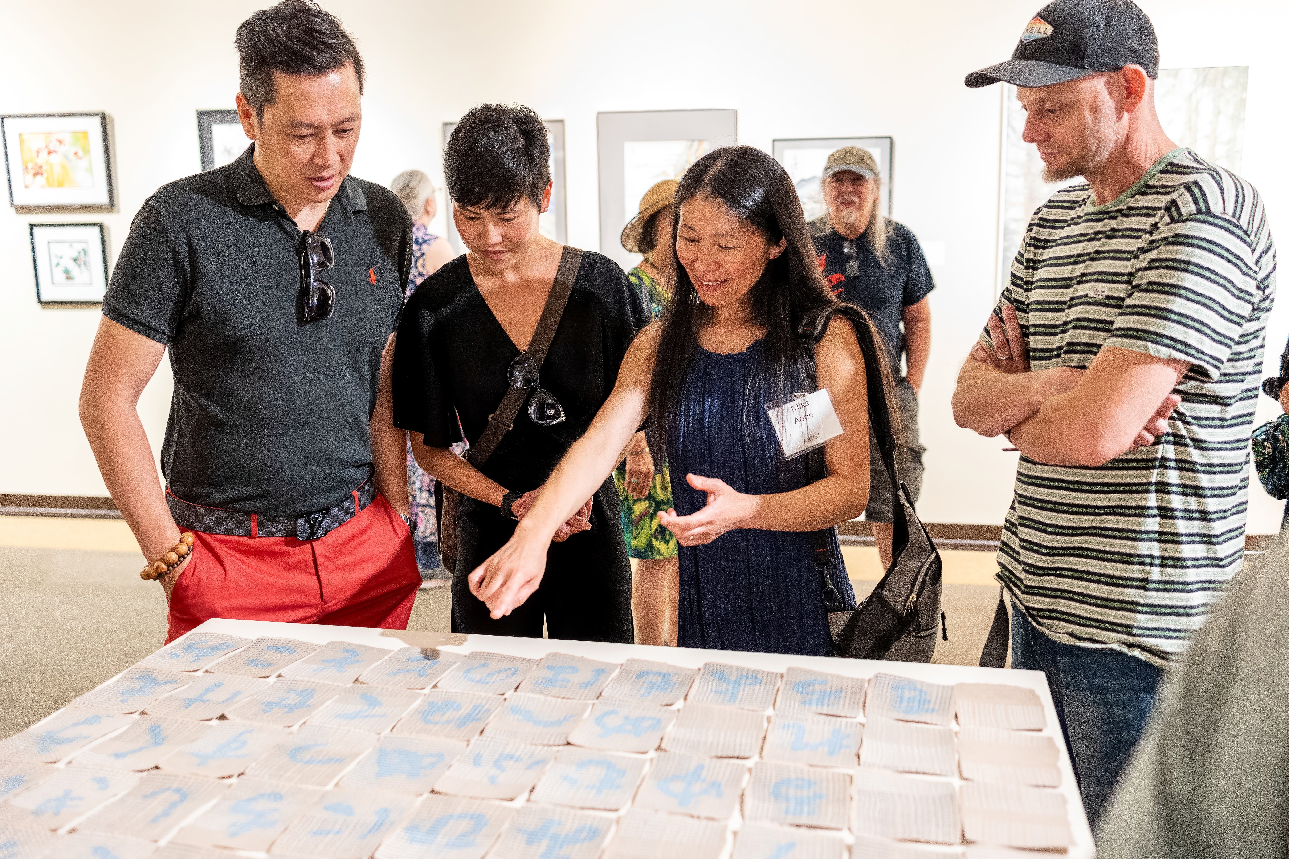 A group of four people look at small paper artworks displayed on a table. 