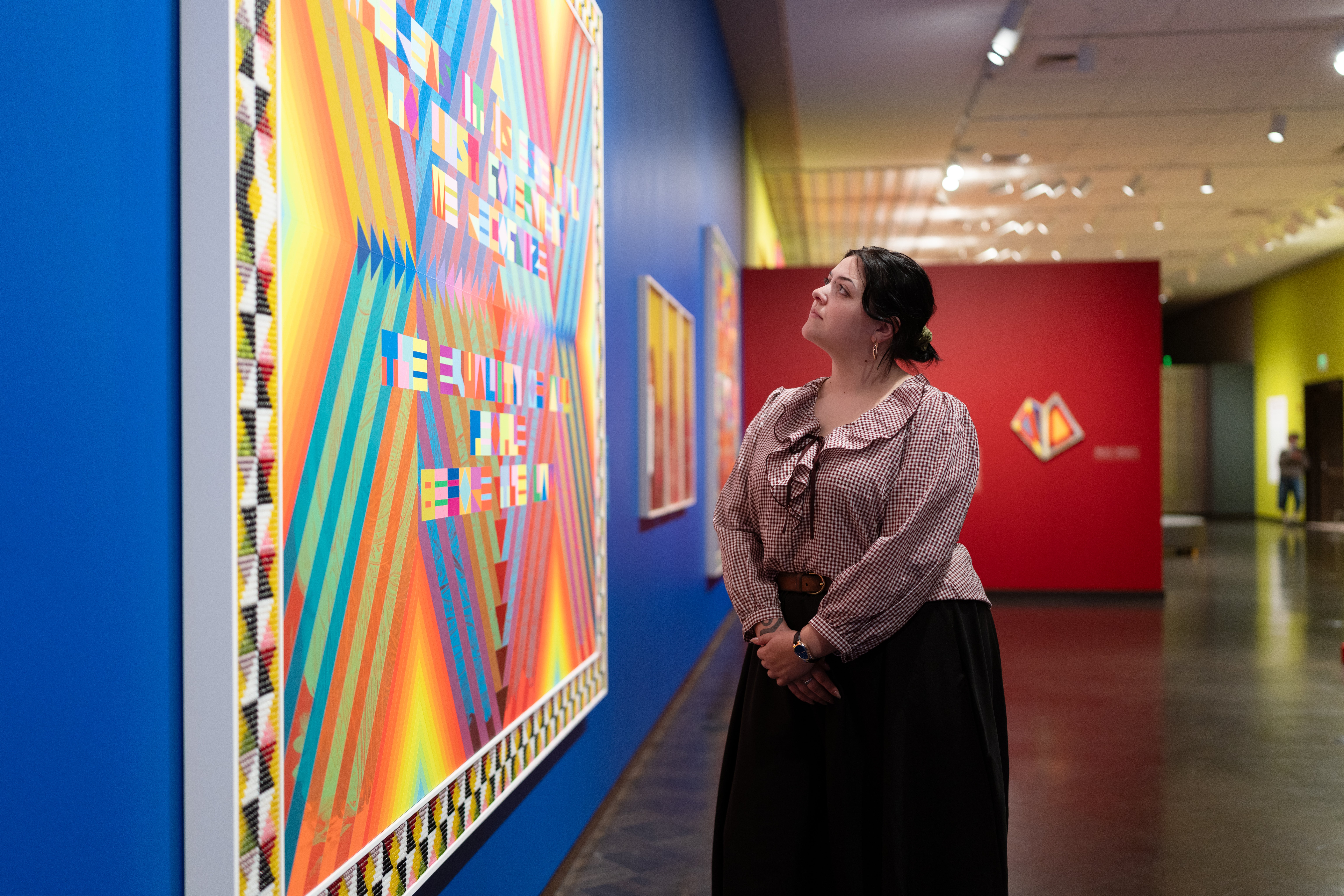 Women looks up at colorful work by Jeffrey Gibson