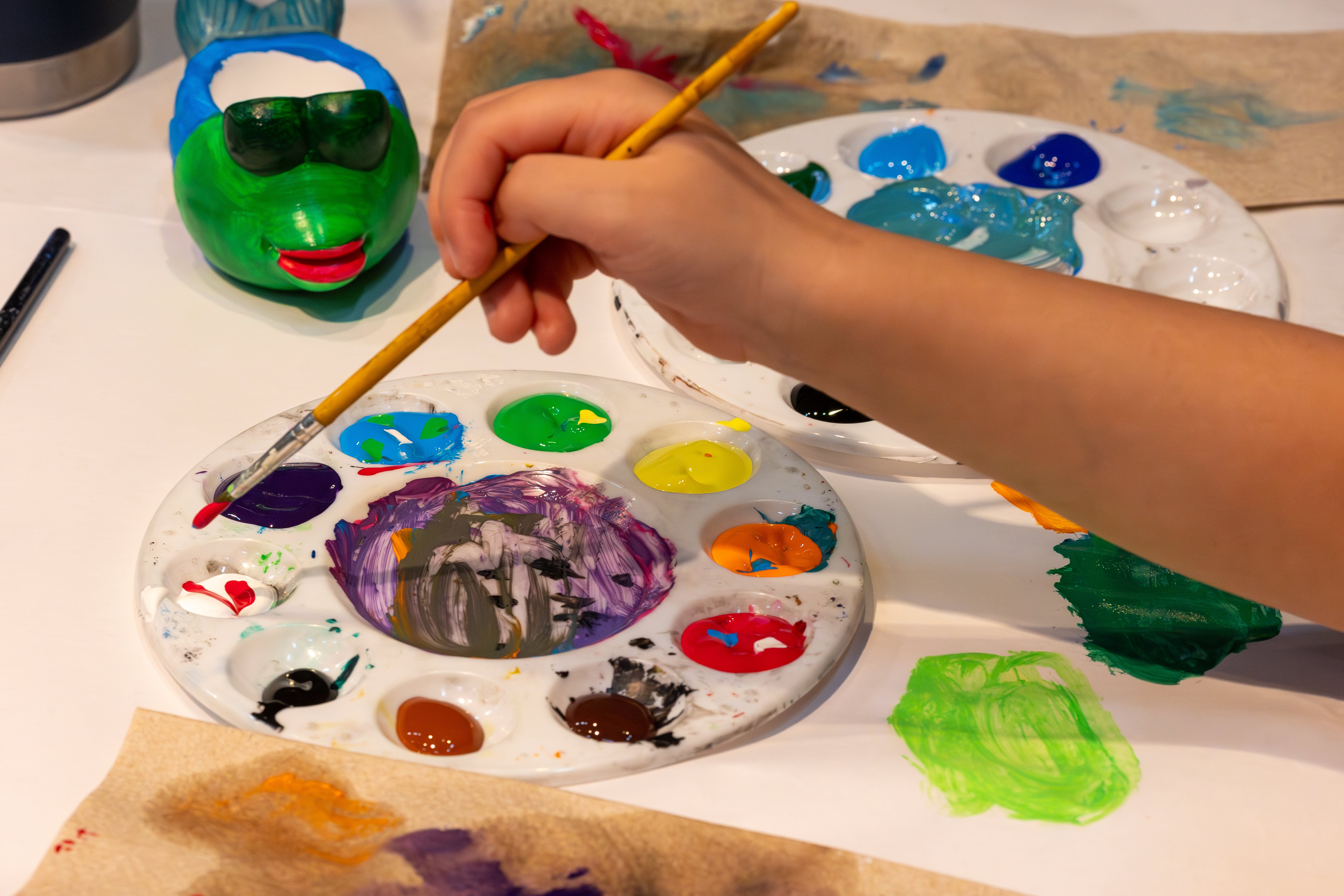 A child's hands dip a paint brush into paint.