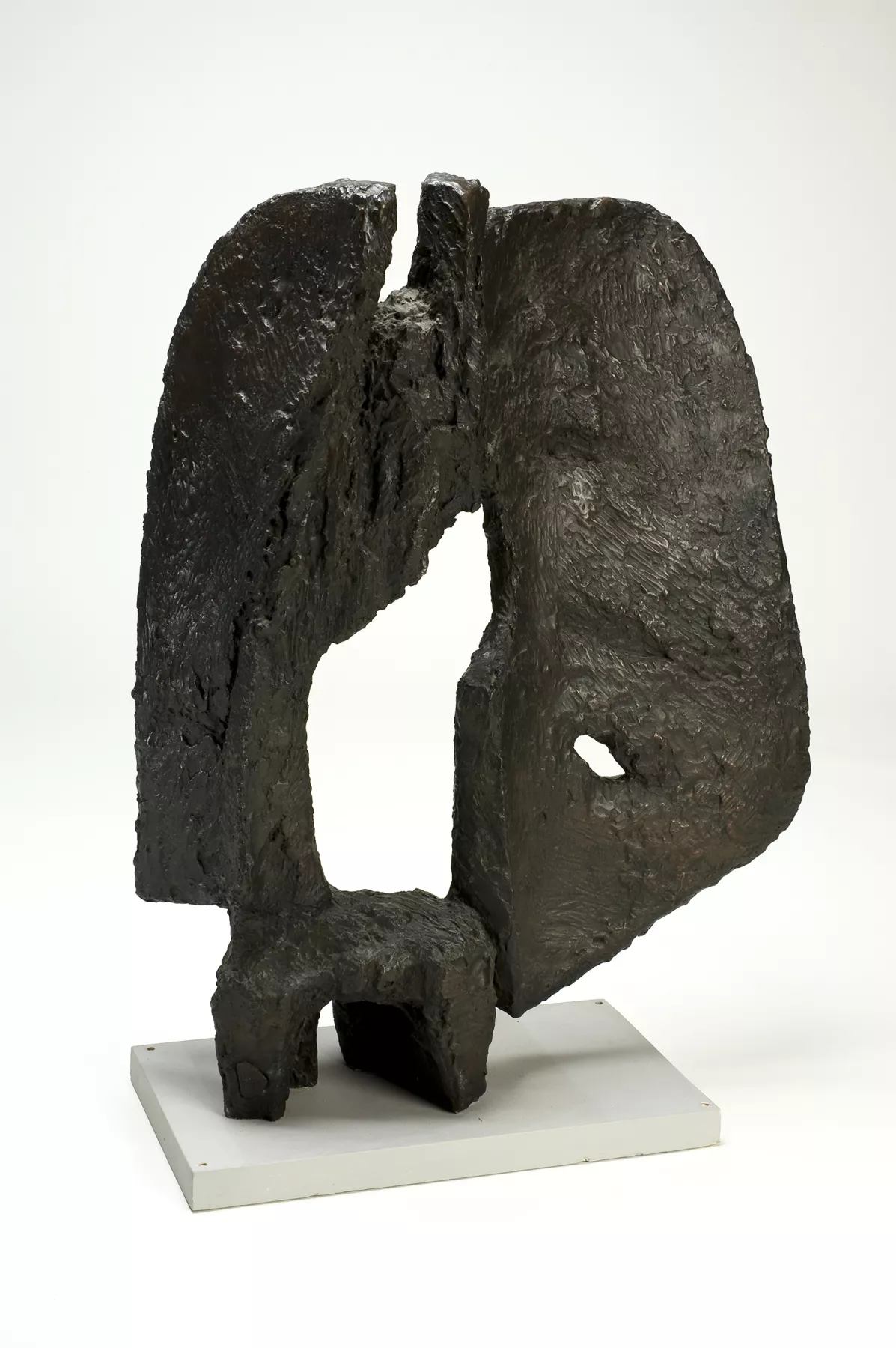 A bronze abstract sculpture with a rough texture and an organic form, featuring a central cut-out section, mounted on a simple white rectangular base.