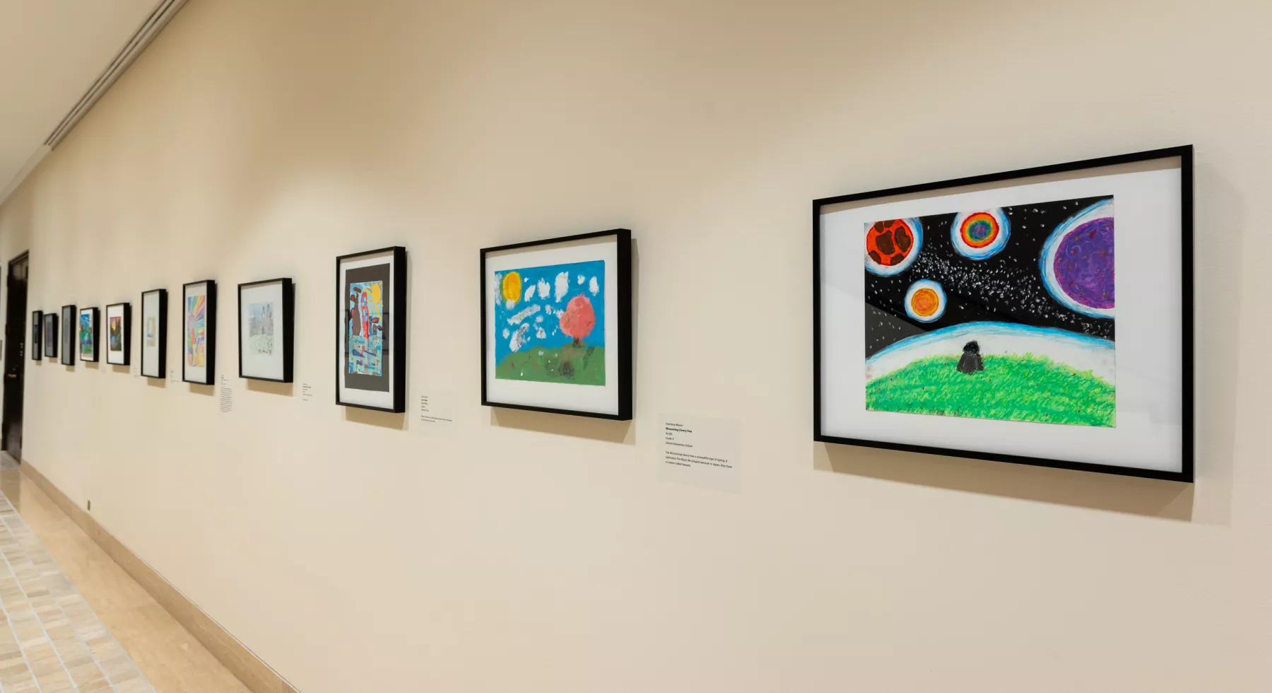 Yellow wall in a hallway with a line of framed kids drawings heading off into the distance.