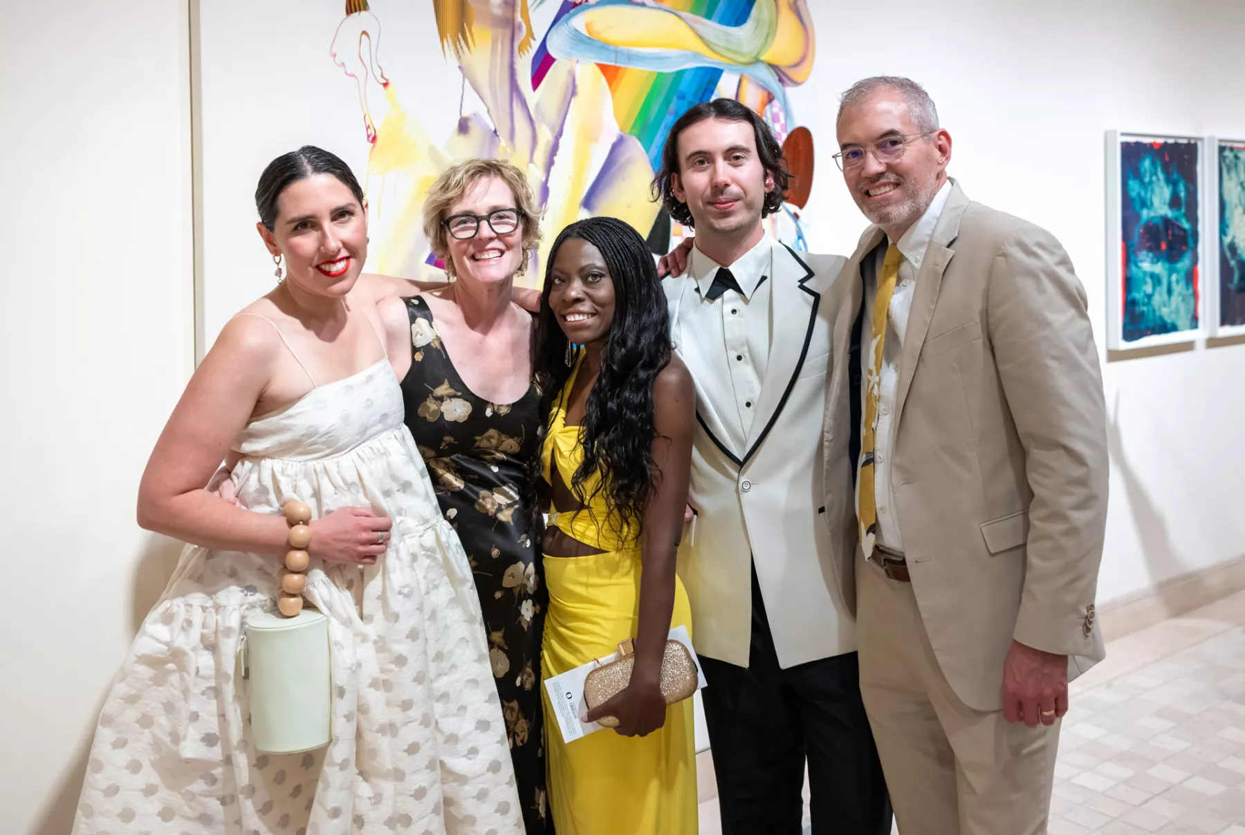 Three women and two men pose for a photograph in front of art.