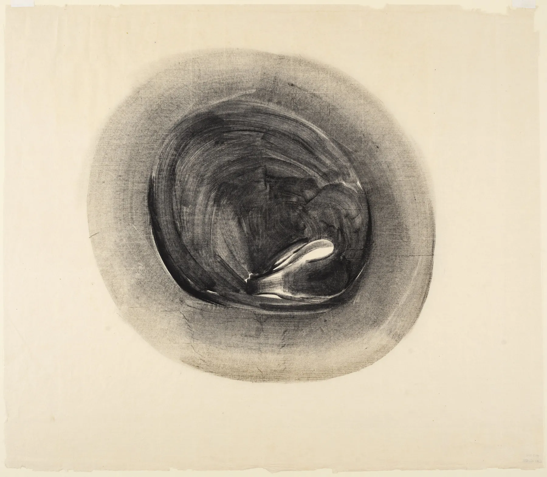 A charcoal or graphite drawing on paper depicting an abstract, organic form resembling a curled-up shape within a circular boundary. The dark, swirling lines create depth and a sense of movement, with areas of soft shading blending into the surrounding space. The composition has a meditative quality, emphasizing texture and tonal contrast against the aged, off-white paper background. The edges of the paper are slightly frayed, adding to the artwork’s tactile presence.